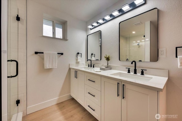 full bathroom with double vanity, a shower stall, a sink, and wood finished floors