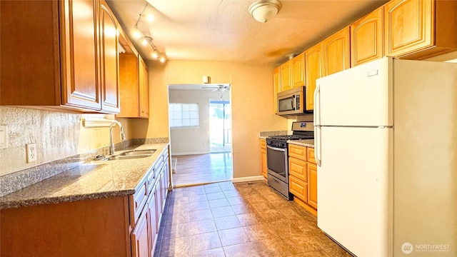 kitchen featuring baseboards, ceiling fan, stainless steel appliances, stone counters, and a sink