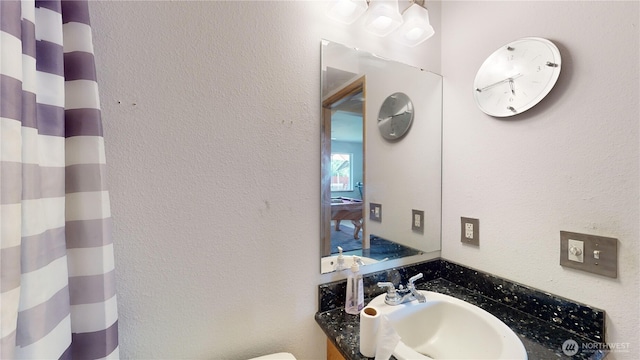 bathroom featuring toilet, a textured wall, a shower with curtain, and vanity