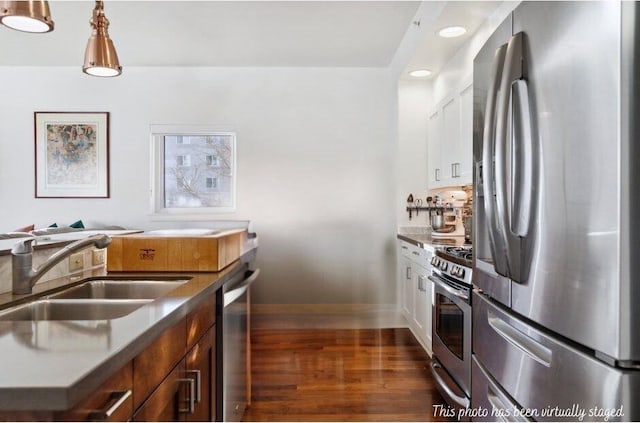 kitchen with stainless steel appliances, dark wood-style flooring, a sink, white cabinets, and baseboards