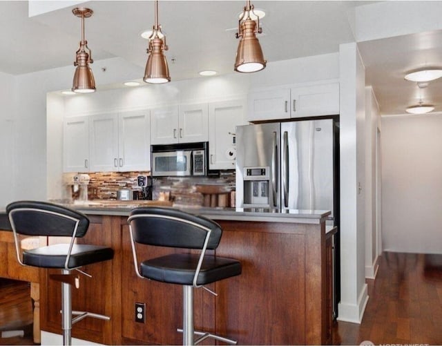 kitchen with appliances with stainless steel finishes, pendant lighting, white cabinets, and backsplash