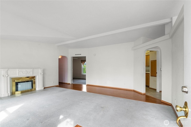 unfurnished living room featuring a fireplace with flush hearth, wood finished floors, arched walkways, and carpet floors