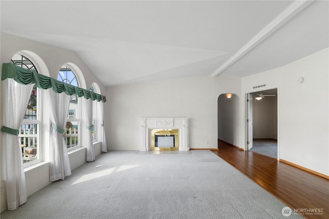 unfurnished living room with wood finished floors, baseboards, vaulted ceiling with beams, a fireplace, and arched walkways