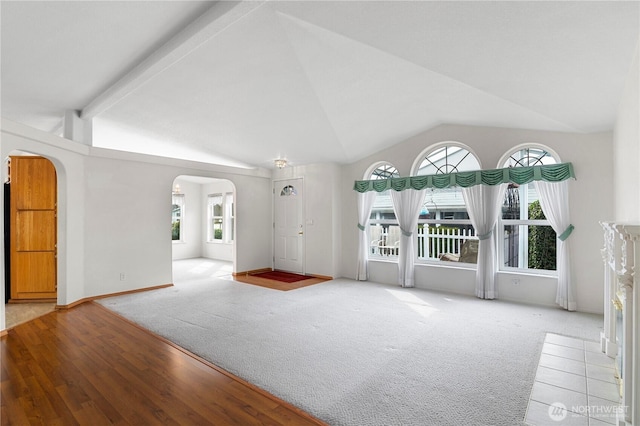 unfurnished living room featuring arched walkways, carpet floors, a fireplace, baseboards, and vaulted ceiling with beams