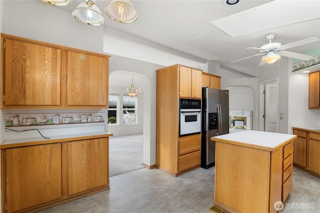 kitchen with light countertops, a skylight, arched walkways, white oven, and stainless steel fridge