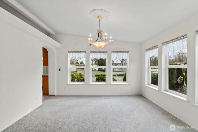 carpeted empty room with baseboards, visible vents, arched walkways, and an inviting chandelier