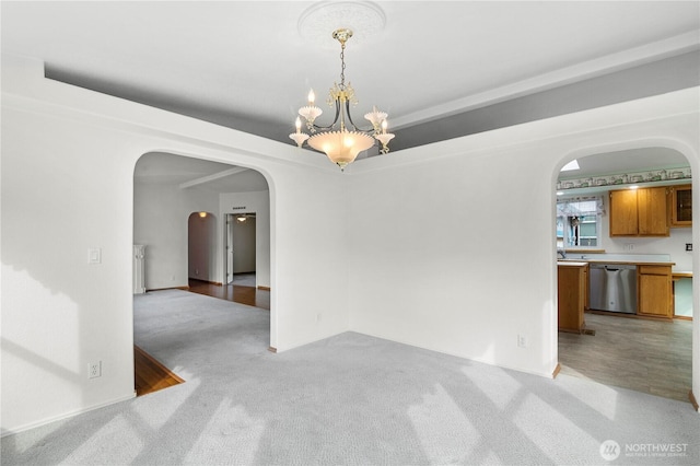 spare room featuring arched walkways, a chandelier, light carpet, and a raised ceiling