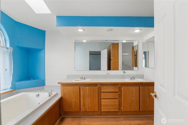 full bathroom featuring double vanity, a skylight, a garden tub, and a sink