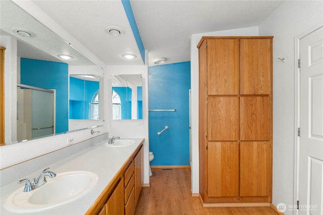 bathroom featuring a sink, toilet, wood finished floors, and a shower stall