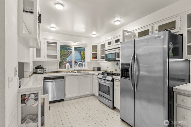 kitchen featuring tile countertops, light floors, stainless steel appliances, white cabinetry, and a sink