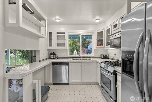 kitchen with stainless steel appliances, white cabinets, a sink, and light floors