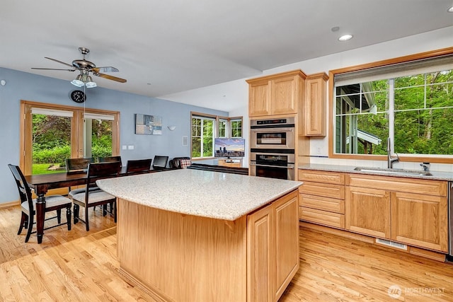 kitchen with visible vents, light wood-style flooring, double oven, a sink, and a kitchen island