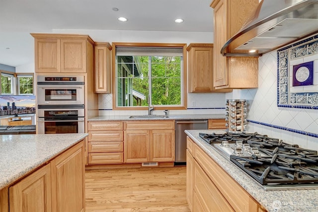 kitchen featuring stainless steel appliances, light wood-style flooring, a sink, wall chimney range hood, and plenty of natural light