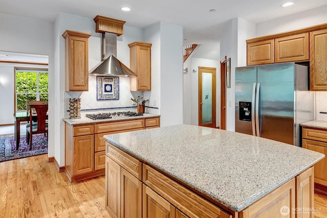 kitchen with light stone counters, a center island, light wood finished floors, stainless steel appliances, and wall chimney exhaust hood