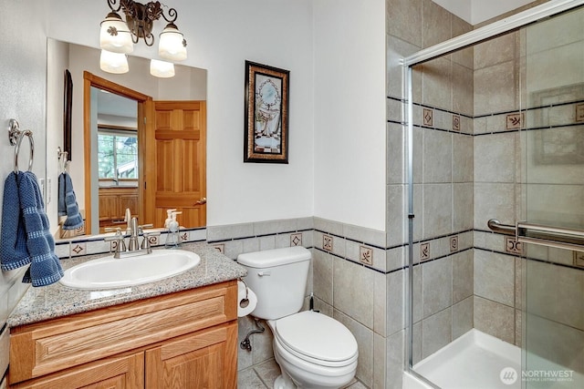 bathroom with a wainscoted wall, tile walls, toilet, a stall shower, and vanity