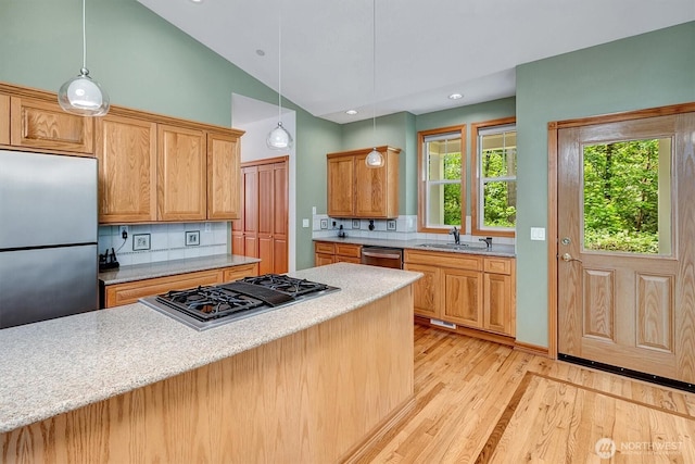 kitchen featuring a sink, vaulted ceiling, appliances with stainless steel finishes, light wood-type flooring, and decorative backsplash