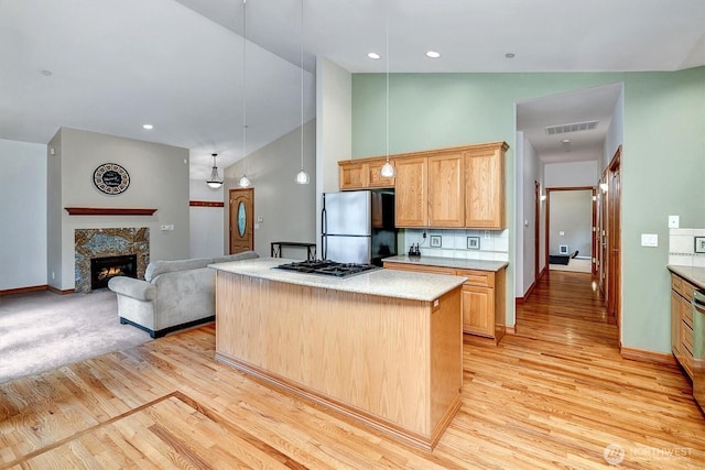 kitchen featuring a center island, stainless steel appliances, visible vents, light wood-style flooring, and a stone fireplace