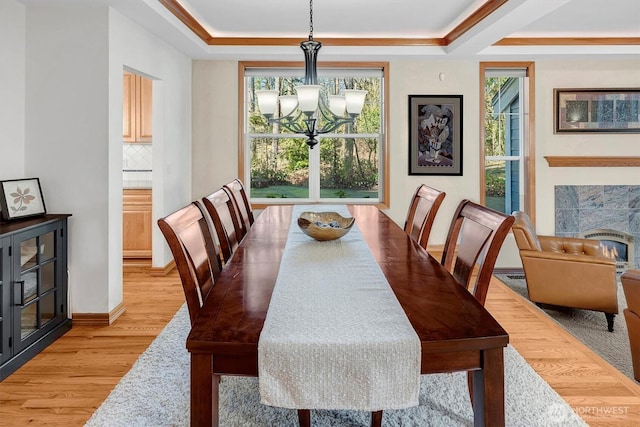 dining space featuring light wood finished floors, a premium fireplace, a raised ceiling, and a notable chandelier