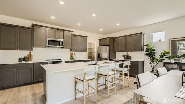 kitchen featuring a kitchen island with sink, a sink, a kitchen breakfast bar, dark brown cabinets, and appliances with stainless steel finishes