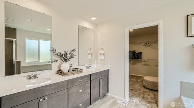 full bathroom featuring double vanity, a shower with door, a walk in closet, and a sink