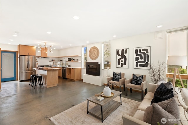 living room with a notable chandelier, recessed lighting, concrete floors, and a fireplace with raised hearth