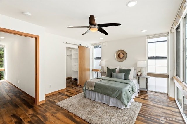 bedroom featuring baseboards, ceiling fan, dark wood finished floors, a barn door, and recessed lighting