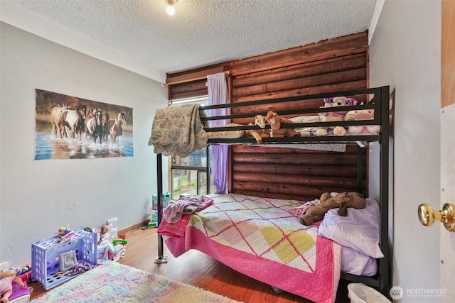 bedroom featuring baseboards, a textured ceiling, log walls, and wood finished floors