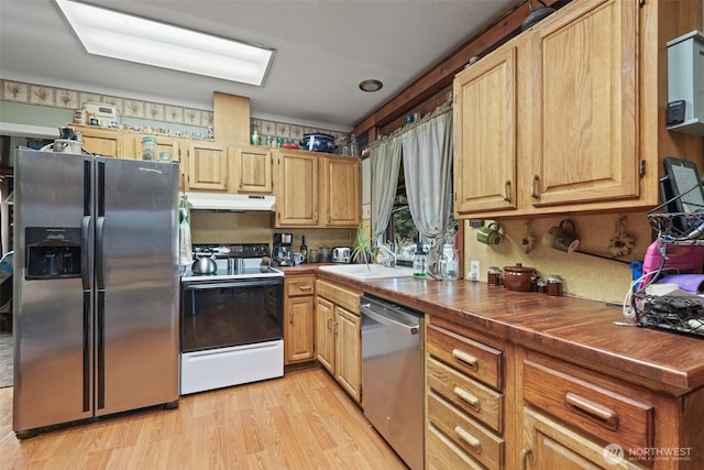 kitchen featuring appliances with stainless steel finishes, light wood-type flooring, a sink, and under cabinet range hood