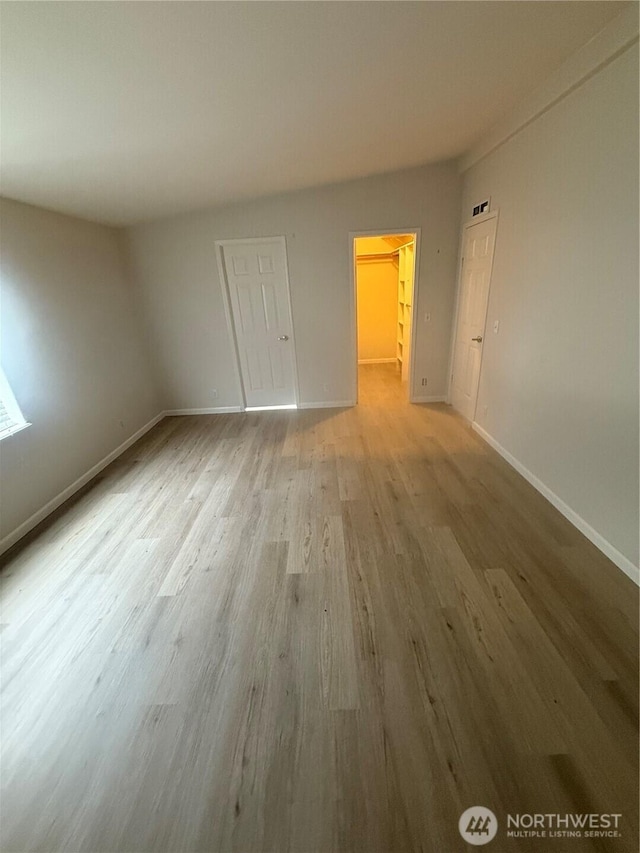 unfurnished bedroom with a spacious closet, wood finished floors, baseboards, and a closet