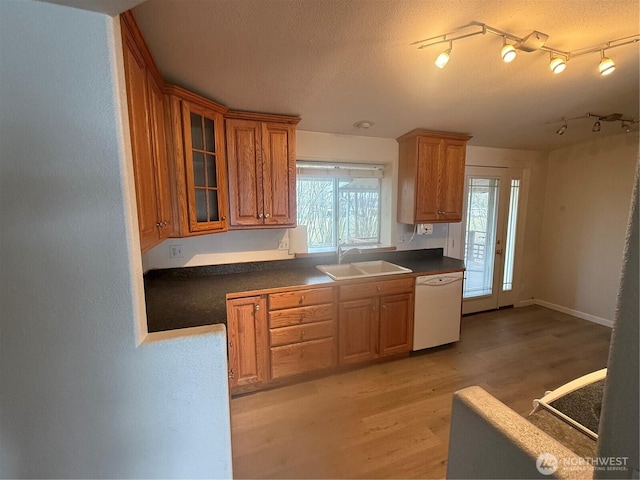 kitchen with light wood-type flooring, brown cabinets, a sink, dark countertops, and white dishwasher