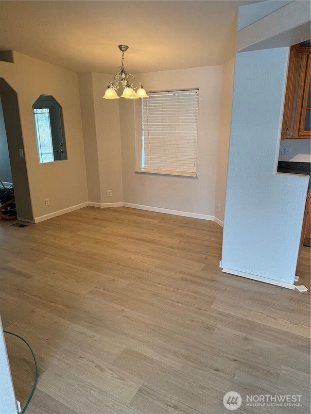 unfurnished dining area featuring light wood-style flooring, a notable chandelier, and baseboards