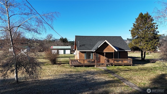 view of front of home with a front lawn, roof with shingles, an outdoor structure, and a wooden deck