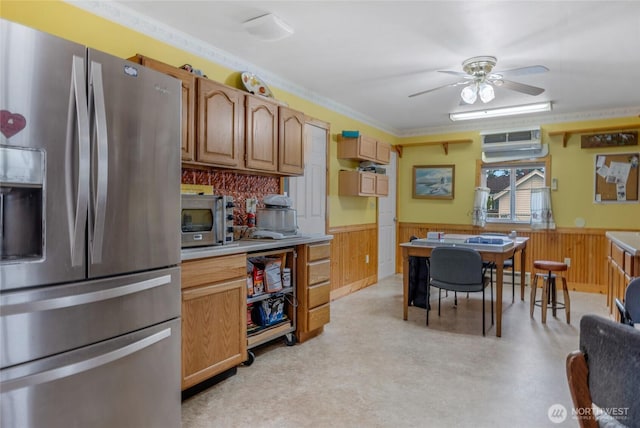 kitchen featuring a ceiling fan, a wainscoted wall, appliances with stainless steel finishes, a wall mounted air conditioner, and light countertops