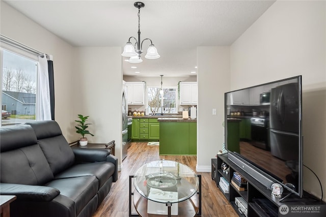 living area featuring baseboards, light wood finished floors, recessed lighting, and a notable chandelier