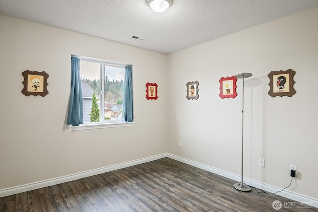 unfurnished room featuring baseboards, visible vents, dark wood finished floors, and a textured ceiling