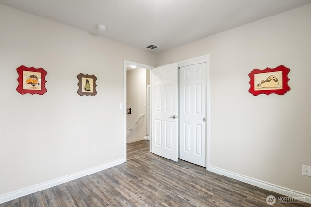 unfurnished bedroom with dark wood-type flooring, a closet, visible vents, and baseboards