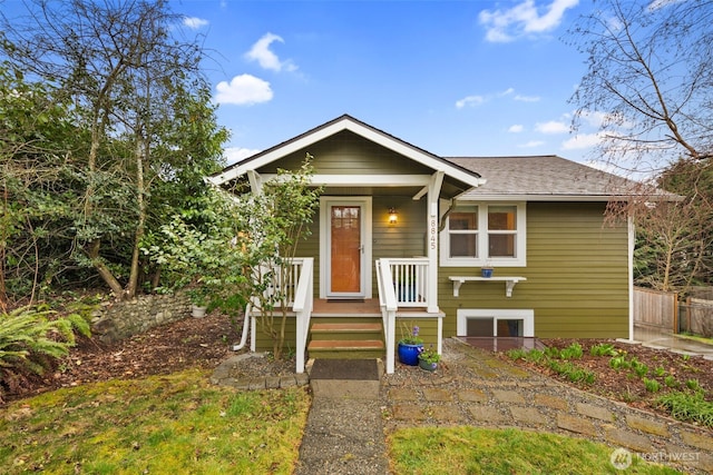 bungalow-style house featuring covered porch, fence, and roof with shingles