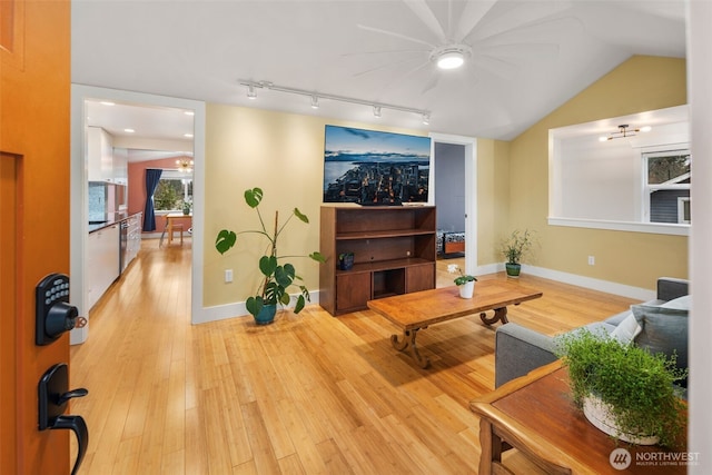 living room with light wood-type flooring, rail lighting, baseboards, and vaulted ceiling