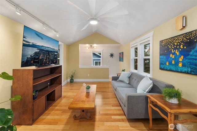 living area with lofted ceiling, light wood finished floors, baseboards, and track lighting