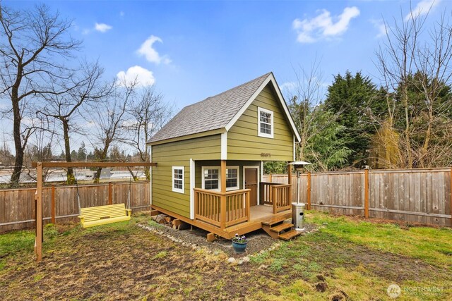 rear view of house featuring a fenced backyard, an outdoor structure, roof with shingles, and a deck