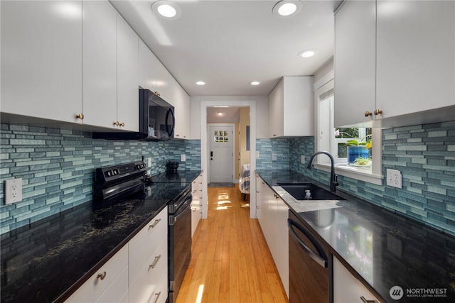 kitchen with backsplash, a sink, light wood-style floors, black appliances, and white cabinetry