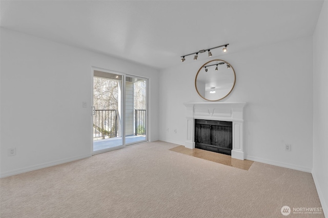 unfurnished living room with rail lighting, carpet, baseboards, and a fireplace with flush hearth