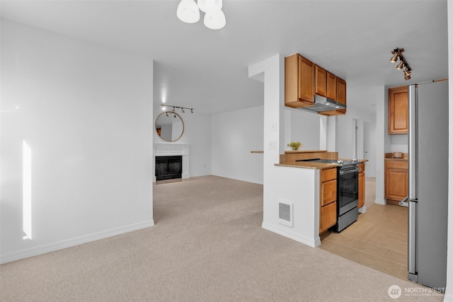 kitchen with brown cabinets, electric range, a fireplace with flush hearth, freestanding refrigerator, and light carpet