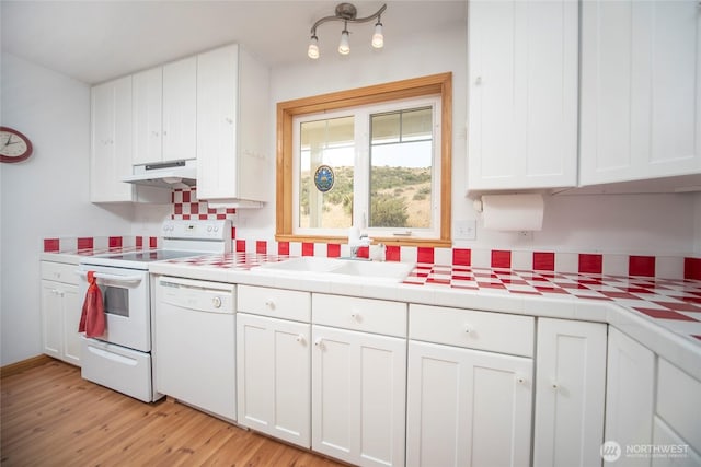 kitchen with white appliances, light wood-style floors, under cabinet range hood, white cabinetry, and a sink