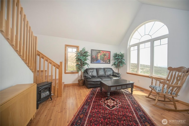 sitting room featuring a wood stove, high vaulted ceiling, light wood-style flooring, and baseboards