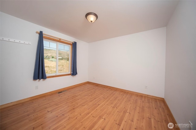 empty room featuring wood-type flooring, visible vents, and baseboards