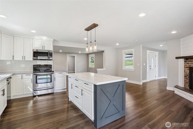kitchen featuring a kitchen island, backsplash, a brick fireplace, stainless steel appliances, and white cabinetry