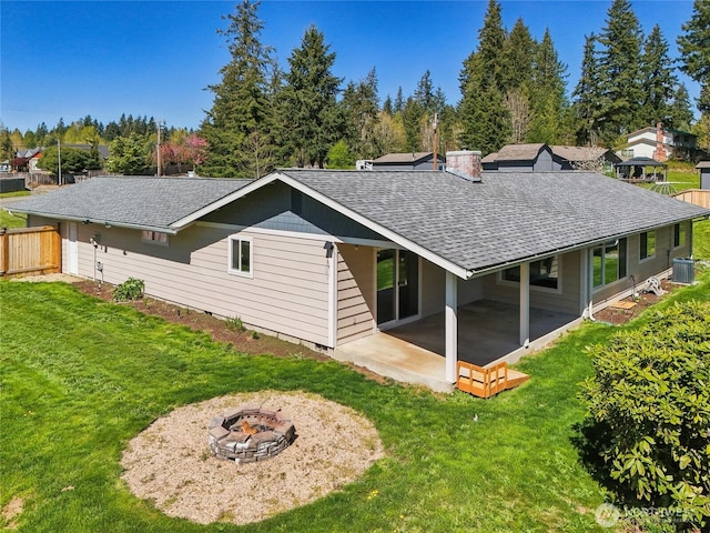 back of house featuring a shingled roof, central air condition unit, a patio, a lawn, and a fire pit
