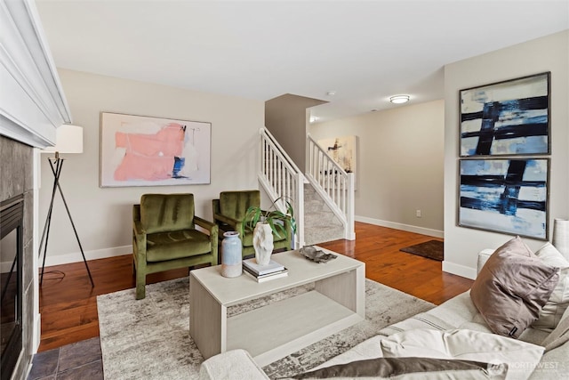 living room with a tile fireplace, stairs, baseboards, and wood finished floors