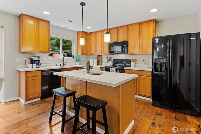 kitchen featuring a kitchen island, wood finished floors, black appliances, and a sink